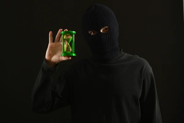 Bandido em máscara preta com ampulheta isolada em preto — Fotografia de Stock