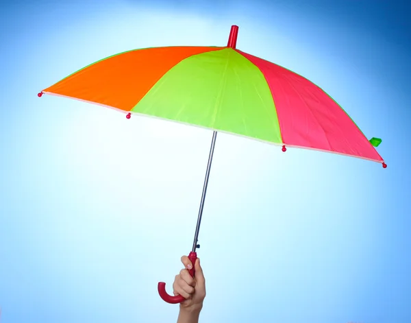 Paraguas multicolor en la mano sobre fondo azul — Foto de Stock