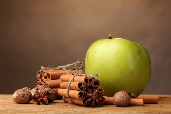 Cinnamon sticks, green apple, nutmeg and anise on wooden table on brown bac — Stock Photo, Image