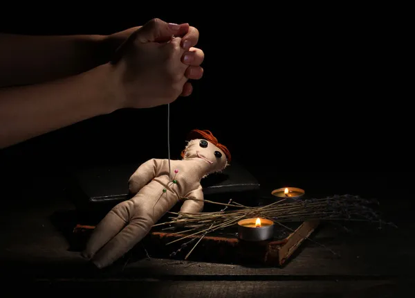Кукла вуду, проколотая иглой на деревянном столе при свете свечей — стоковое фото