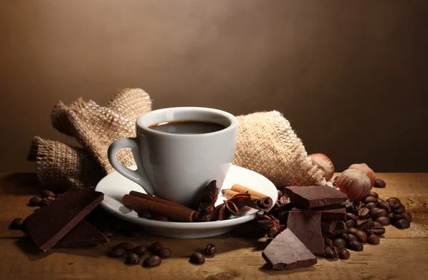 Coffee cup and beans, cinnamon sticks, nuts and chocolate on wooden table o — Stock Photo, Image