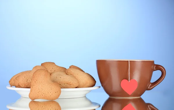 Heart-shaped cookies on plate and cup with tea bag on blue background — Stock Photo, Image