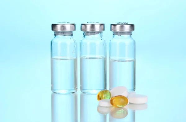 Tabletas y ampollas sobre fondo azul — Foto de Stock