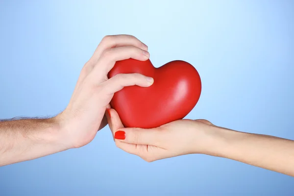 Man and woman holding red heart in hands on blue background — Stock Photo, Image