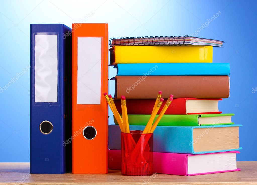 Bright office folders and books with stationery on wooden table on blue bac