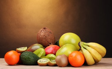 Assortment of exotic fruits on wooden table on brown background clipart