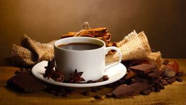 Coffee cup and beans, cinnamon sticks, nuts and chocolate on wooden table o clipart