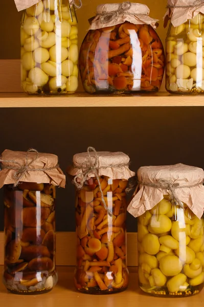 Deliciosos champiñones marinados en los frascos de vidrio en estantes de madera — Foto de Stock