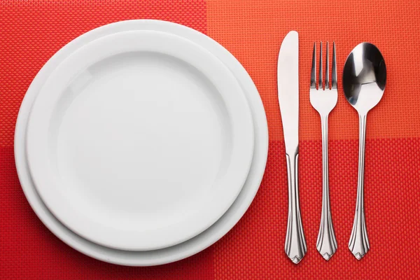 Placa vazia branca com garfo, colher e faca em uma toalha de mesa vermelha — Fotografia de Stock