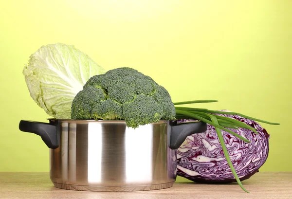 Saucepan dengan brokoli dan kubis di atas meja kayu dengan latar belakang hijau — Stok Foto