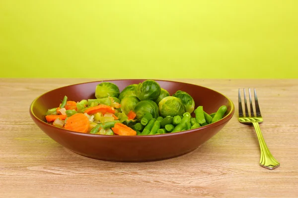 Mixed vegetables on plate on wooden table on green background — Stock Photo, Image