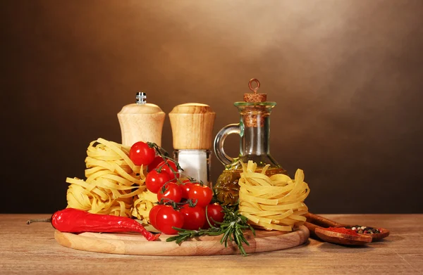 Noedels in bowl, pot van olie, kruiden en groenten op houten tafel op brown — Stockfoto