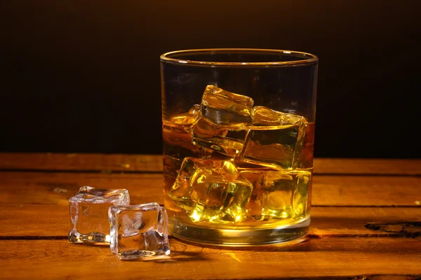 Vidro de uísque e gelo na mesa de madeira sobre fundo marrom — Fotografia de Stock