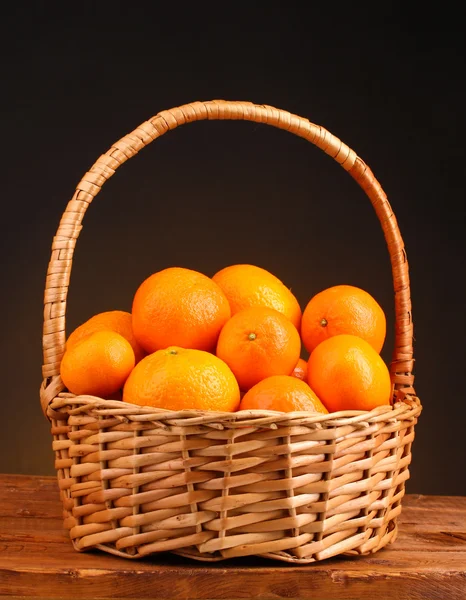 Tangerines in a beautiful basket on wooden table on brown background — Stock Photo, Image