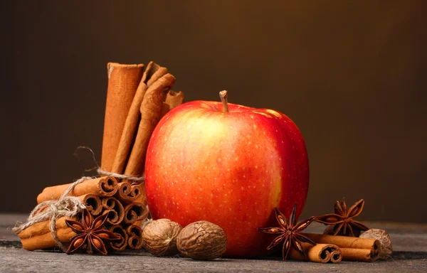 Palitos de canela, manzana roja, nuez moscada y anís sobre mesa de madera sobre fondo marrón — Foto de Stock