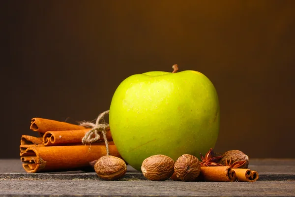 Cinnamon sticks, green apple and nutmeg on wooden table on brown background — Stock Photo, Image