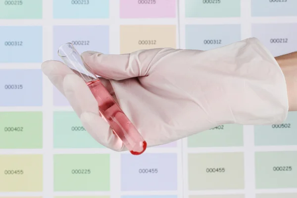 Tubo con líquido rosa en la mano en el fondo de muestras de color — Foto de Stock