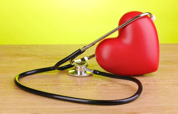 Estetoscopio médico y corazón sobre mesa de madera sobre fondo verde —  Fotos de Stock