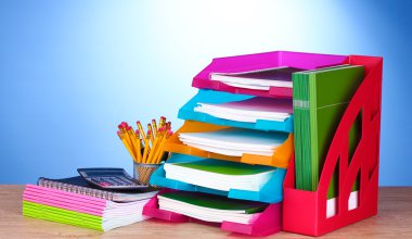 Bright paper trays and stationery on wooden table on blue background clipart