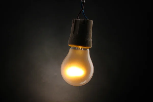 Uma lâmpada acesa sobre fundo cinzento — Fotografia de Stock