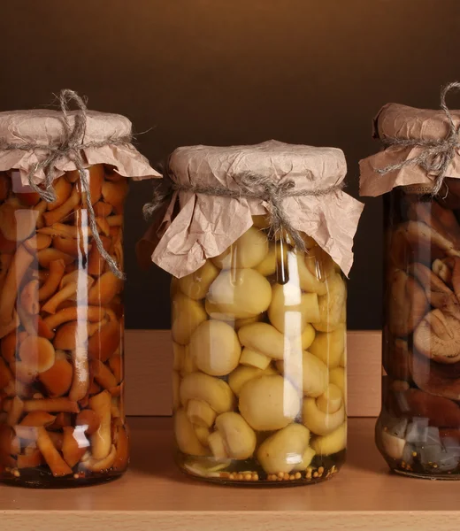 Köstliche marinierte Pilze in den Glasgefäßen auf Holzregalen — Stockfoto
