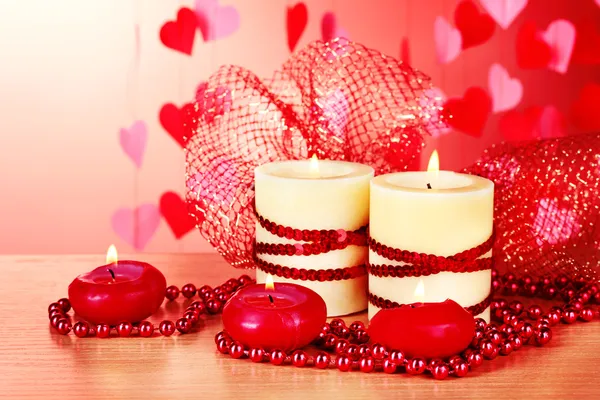 Hermosas velas con una decoración romántica sobre una mesa de madera sobre un fondo rojo — Foto de Stock
