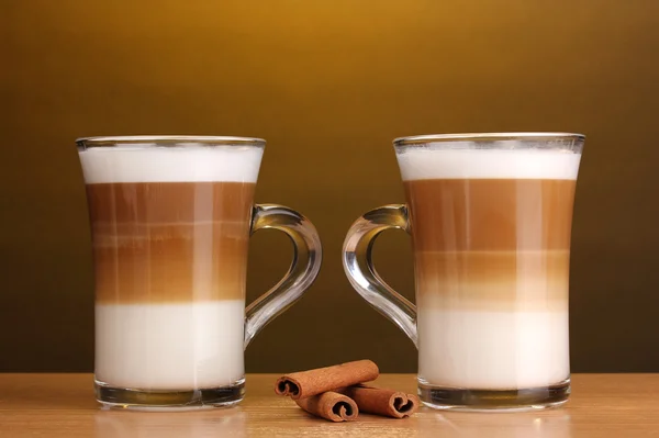 Duftender Kaffee-Latte in Glasbechern und Zimt auf Holztisch auf braunem B — Stockfoto