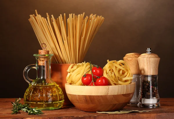 Spaghetti, makaron w misce, słoik oleju i warzywa na drewnianym stole na br — Zdjęcie stockowe