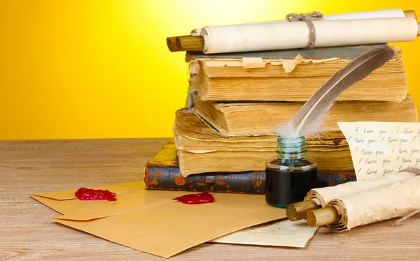 Oude boeken, rollen, veer pen en inktpotje op houten tafel op gele backg — Stockfoto