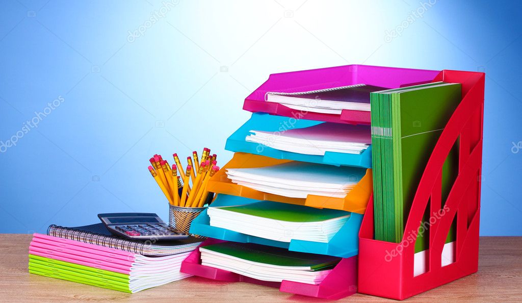 Bright paper trays and stationery on wooden table on blue background