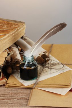 Old books, scrolls, feather pen and inkwell on wooden table on grey backgro clipart