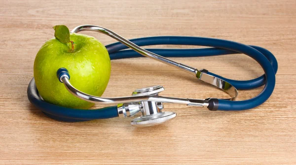 Ιατρική στηθοσκόπιο και πράσινο μήλο σε ξύλινα φόντο — Φωτογραφία Αρχείου