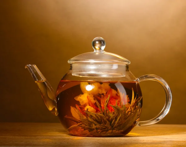 Szklany czajniczek z egzotycznych zielonej herbaty na drewnianym stole na brązowym tle — Zdjęcie stockowe