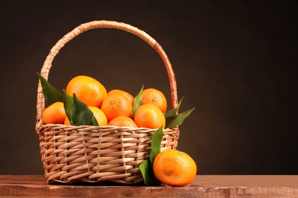 Mandarinas con hojas en una hermosa canasta sobre mesa de madera sobre respaldo marrón —  Fotos de Stock