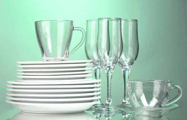 Чистые тарелки, чашки и очки на зеленом фоне — стоковое фото