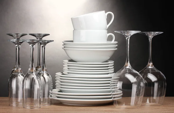 Чисті тарілки, окуляри та чашки на дерев'яному столі на сірому фоні — стокове фото