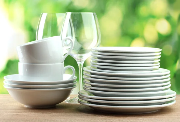 Clean dishes on wooden table on green background — Stock Photo, Image
