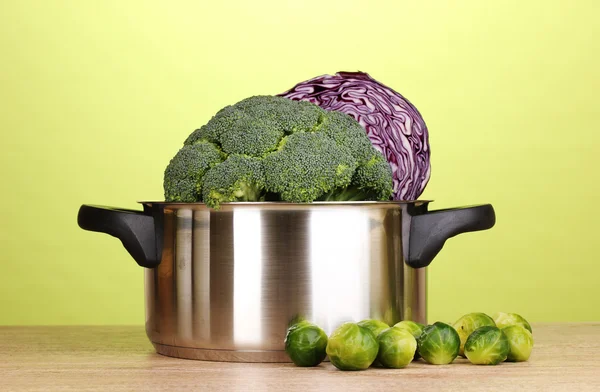 Saucepan with cabbages and broccoli on wooden table on green background — Stock Photo, Image