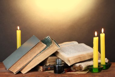 Old books, scrolls, ink pen inkwell and candles on wooden table on brown ba clipart