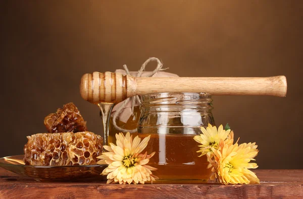 Dos tarros de miel, panales de miel y llovizna de madera en la mesa sobre fondo amarillo — Foto de Stock