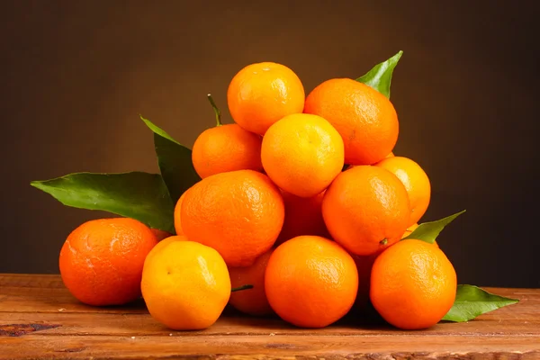 Tangerines avec feuilles sur table en bois sur fond marron — Photo