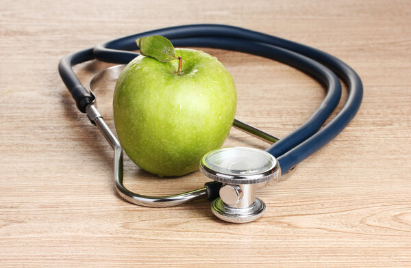 Medical stethoscope and green apple on wooden background