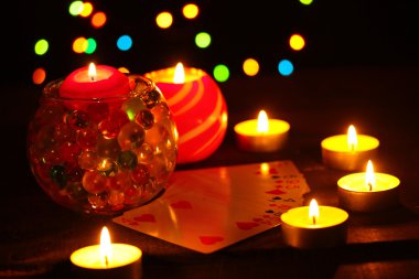 Candles and playing cards on wooden table on bright background clipart