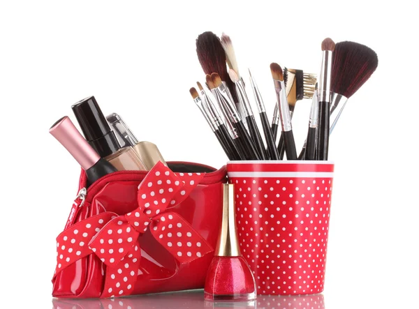 Vidrio rojo con cepillos y bolsa de maquillaje con cosméticos aislados en blanco —  Fotos de Stock