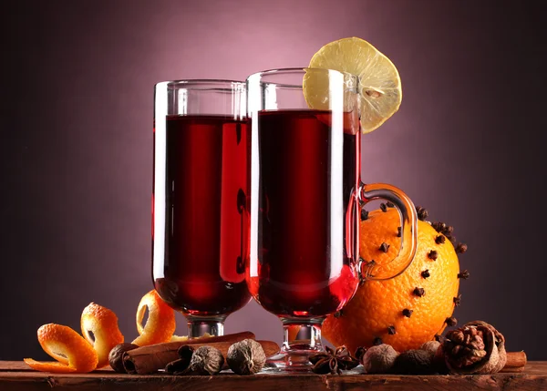 Vino rimuginato nei bicchieri, spezie e arancia sul tavolo di legno sul retro viola — Foto Stock