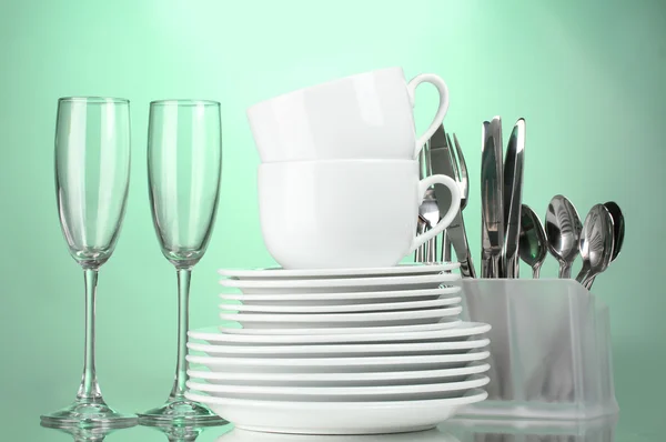Чистые тарелки, стаканы, чашки и столовые приборы на зеленом фоне — стоковое фото