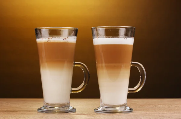 Fragante café con leche en copas de vidrio sobre mesa de madera sobre fondo marrón — Foto de Stock