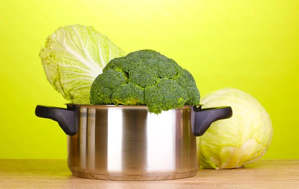 Saucepan dengan brokoli dan kubis di atas meja kayu dengan latar belakang hijau — Stok Foto