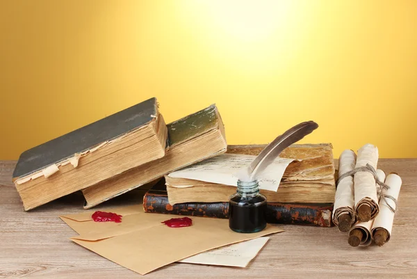 stock image Old books, scrolls, feather pen and inkwell on wooden table on yellow backg