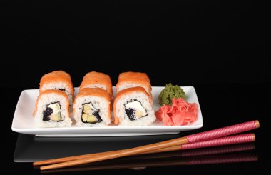 Tasty rolls served on white plate with chopsticks isolated on black clipart